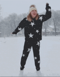 a woman in a black sweater with white stars on it is standing in the snow