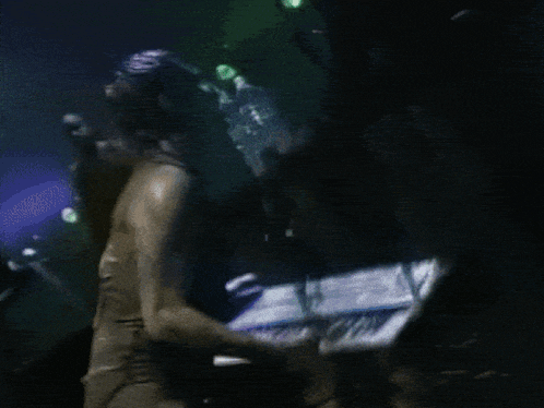 a man playing a keyboard in a dark room with green lights behind him