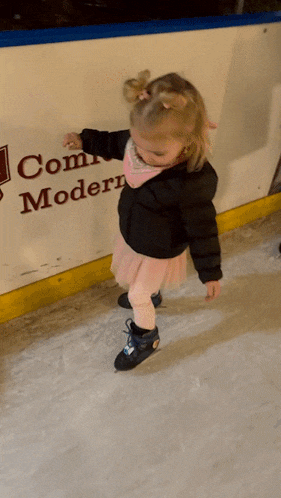 a little girl ice skating in front of a sign that says com modern