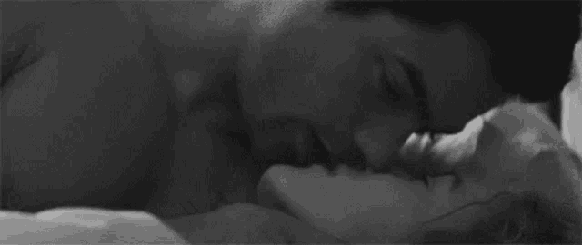 a black and white photo of a man and a woman kissing in bed .