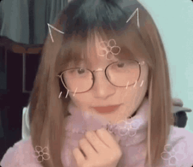 a young girl wearing glasses and a pink sweater is making a heart shape with her hands .