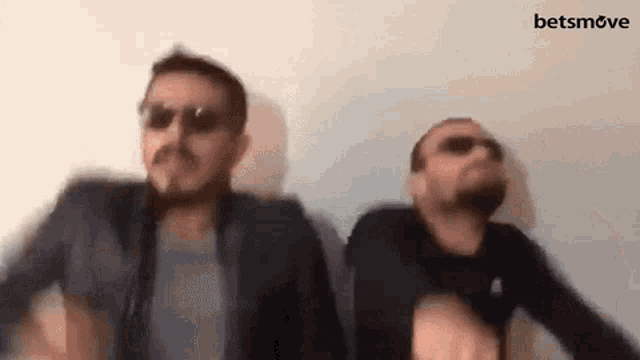 two men wearing sunglasses are dancing in front of a wall and the word betsmove is on the bottom