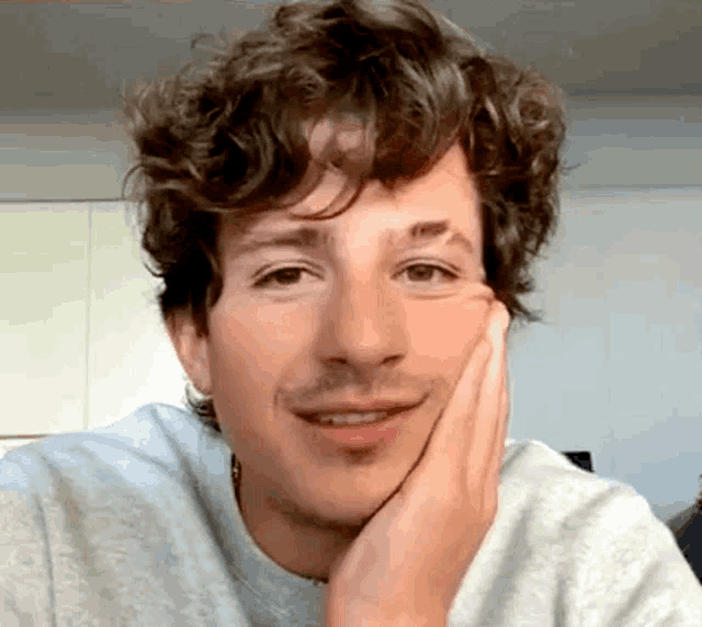 a close up of a man with curly hair and a mustache holding his hand to his face .