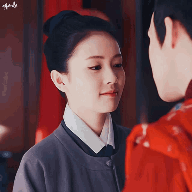 a woman in a gray jacket looks at a man in a red jacket with the word gif on the bottom right