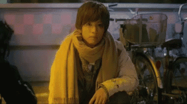 a young man wearing a scarf is sitting in front of a bicycle .