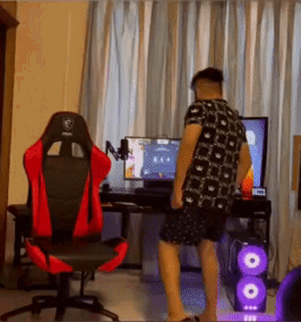 a man in a black and white shirt is standing in front of a computer .