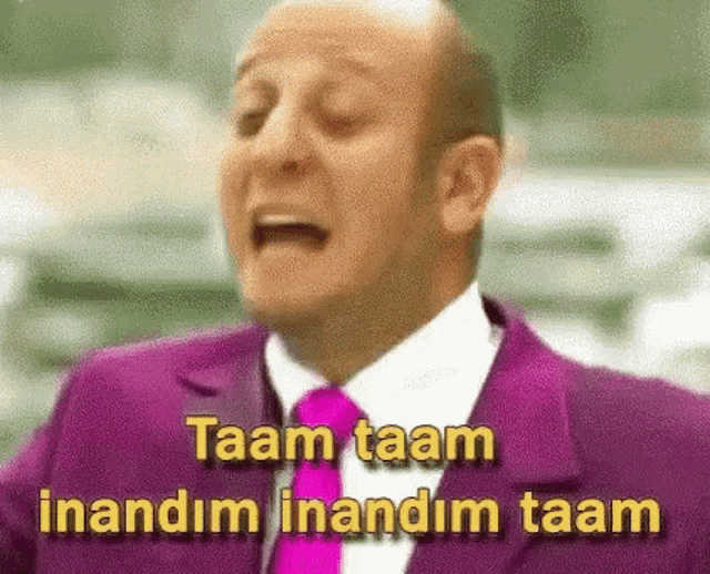 a bald man in a purple suit and pink tie is making a funny face .