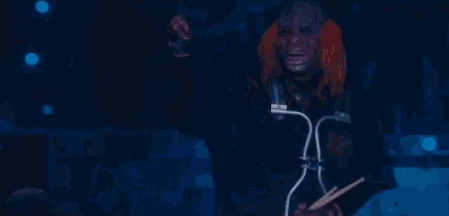 a clown with red hair is playing drums in a dark room .