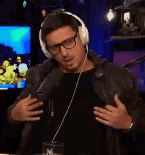 a man wearing headphones and glasses is singing into a microphone while holding his chest .