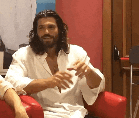 a man with long hair and a beard is sitting in a red chair talking to someone .