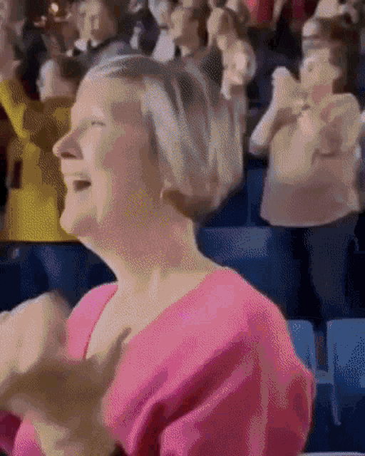 a woman in a pink shirt is laughing in a crowd of people