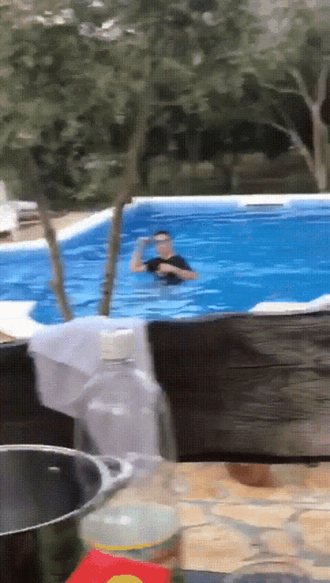a man is swimming in a swimming pool with a bottle of water in the foreground