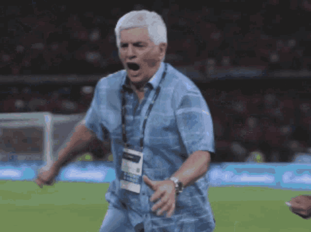 a man in a blue shirt with a lanyard around his neck shouts