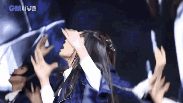 a woman in a blue jacket is covering her face with her hands while dancing in front of a crowd .