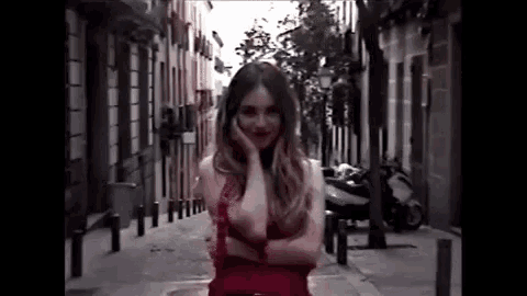 a woman in a red dress is standing in a narrow alleyway .