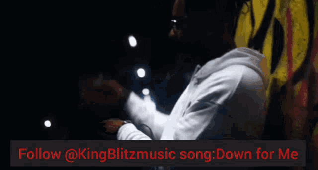 a man is standing in front of a wall with the words follow @kingblitzmusic song down for me on the bottom