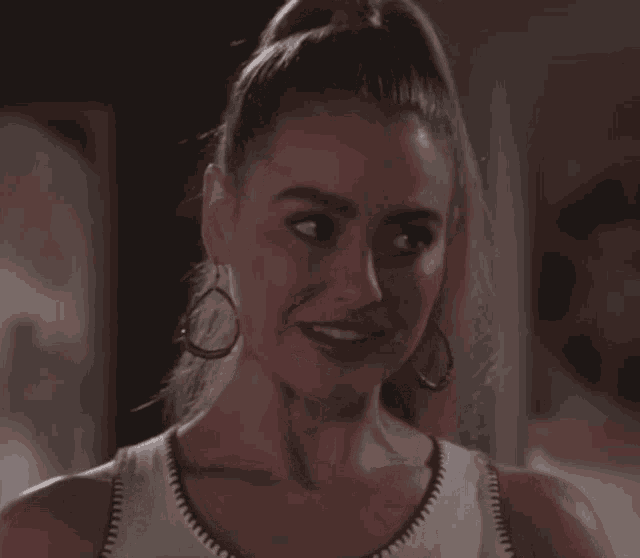a woman with a ponytail and earrings smiles at the camera