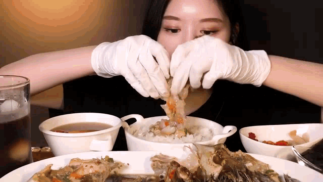 a woman wearing white gloves is eating crabs and rice