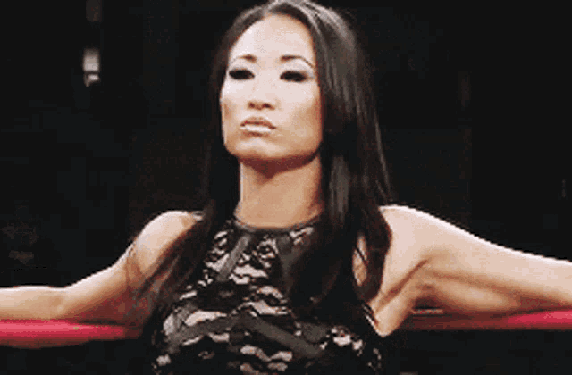 a woman in a black lace dress is standing in a ring with her arms outstretched