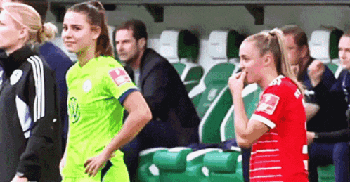 two female soccer players are standing next to each other in a locker room .