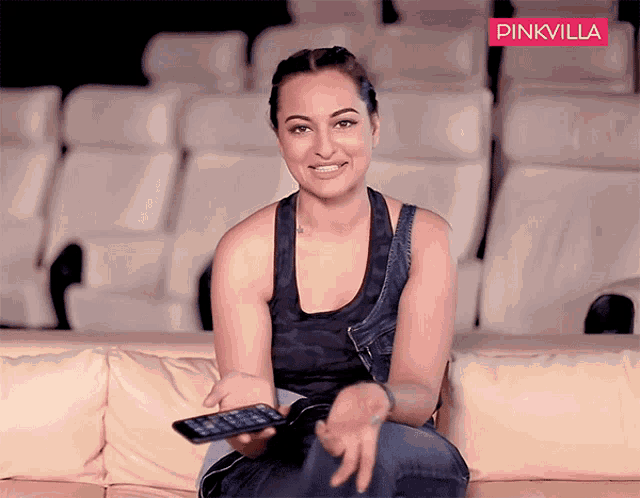 a woman sitting on a couch holding a remote control with a pinkvilla logo in the background