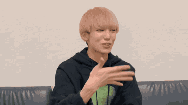 a young man with blonde hair is sitting on a couch with his hands outstretched and smiling .