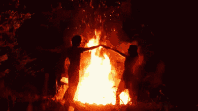 a man and woman are dancing in front of a fire at night