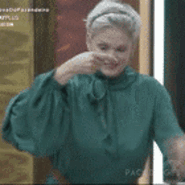 a woman in a green shirt is making a funny face with her hand .