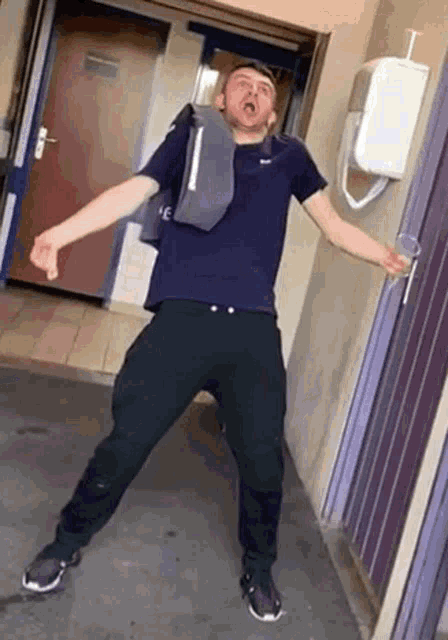 a man in a purple shirt and black pants is standing in front of a door holding a cup .