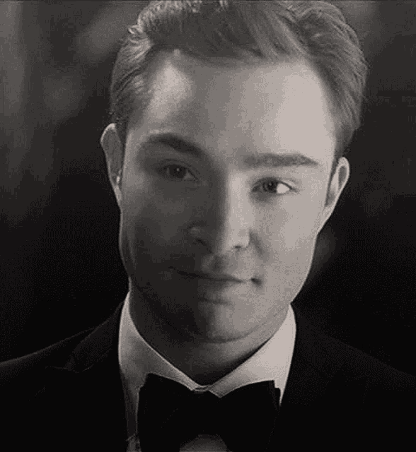 a black and white photo of a man in a tuxedo and bow tie smiling .