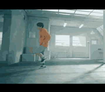 a man in an orange hoodie is dancing in a room