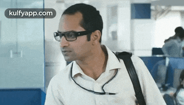 a man wearing glasses and carrying a briefcase is walking in an office .