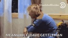 a man in a blue shirt is sitting in front of a window and talking on a phone .