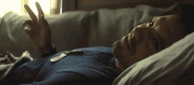 a man in a blue shirt is laying in bed with his eyes closed