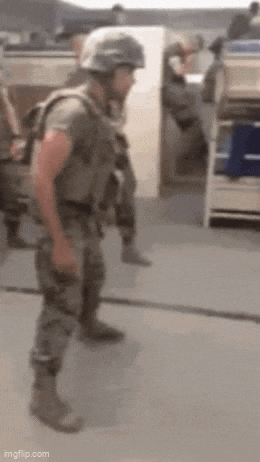 a soldier wearing a helmet and holding a gun is standing on the ground .