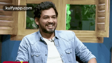 a man in a denim shirt is smiling while sitting in a chair .