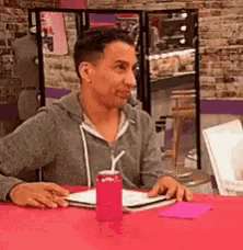a man is sitting at a table with a can of soda and a straw in his mouth .