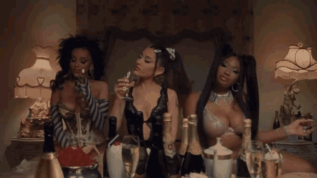 three women are standing around a table with bottles of champagne