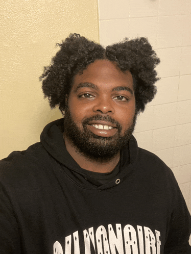 a man with curly hair and a beard wears a black billionaire hoodie