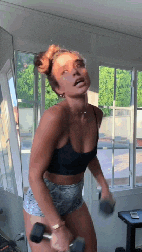 a woman in a black crop top and shorts is holding a dumbbell