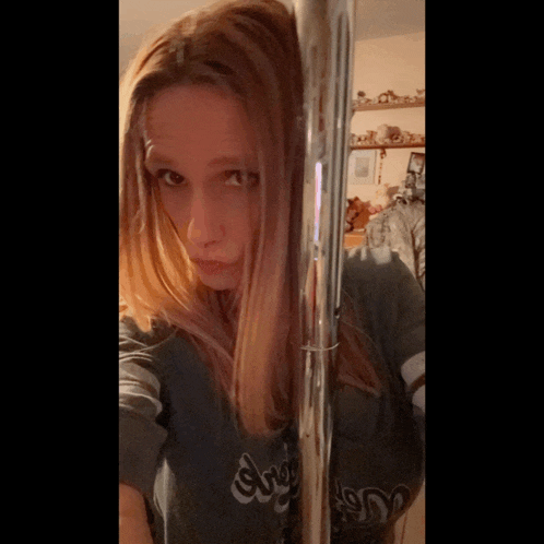 a woman wearing a shirt that says angels is standing next to a metal pole