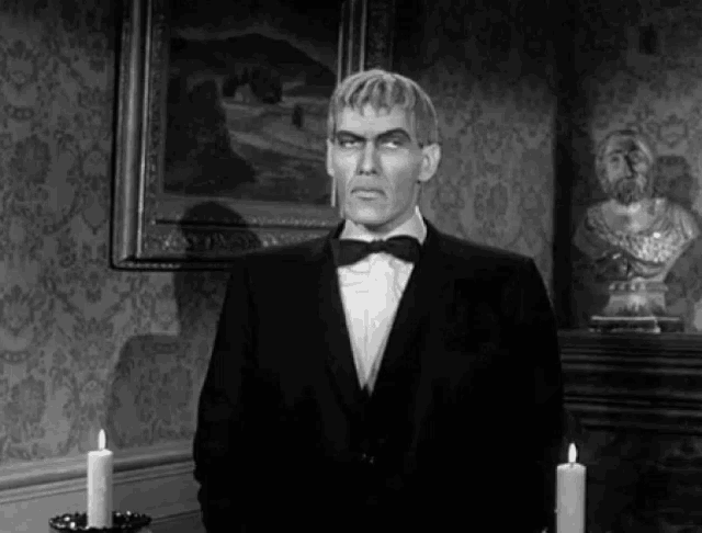 a man in a tuxedo and bow tie is standing in front of candles