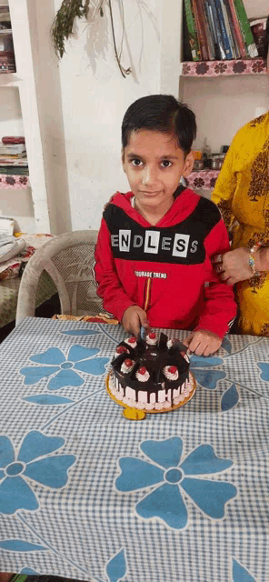 a boy wearing a red endless shirt is cutting a cake