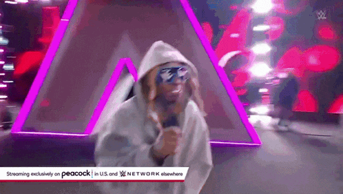 a man wearing a hoodie and sunglasses is singing into a microphone on a stage