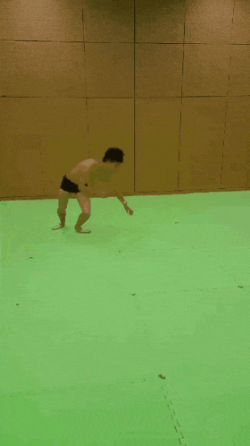 a man without a shirt is doing a handstand on a green mat
