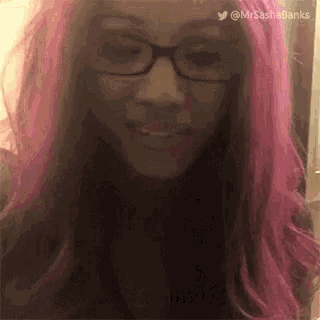 a woman with pink hair and glasses is smiling and looking at the camera .