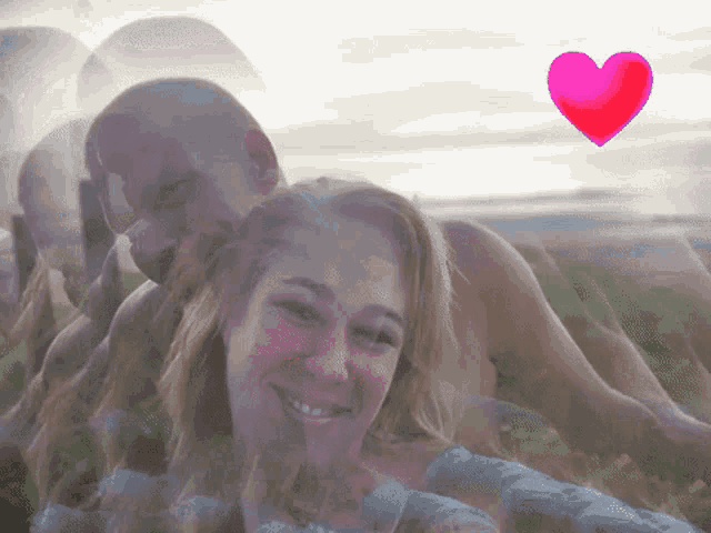 a man and a woman are standing next to each other in a field with a pink heart flying in the background .
