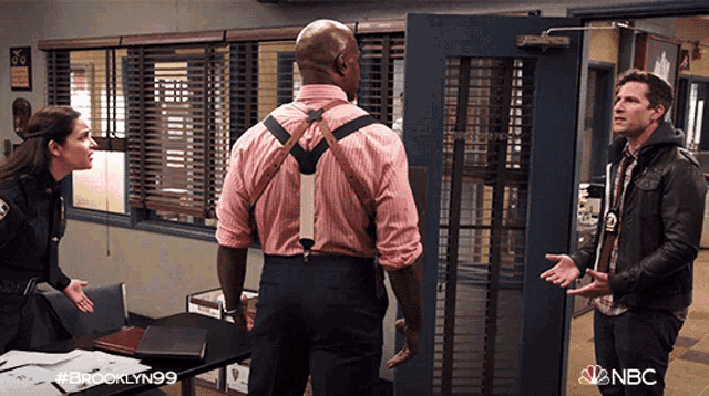 a man in a pink shirt and suspenders is talking to a woman and a man in a leather jacket