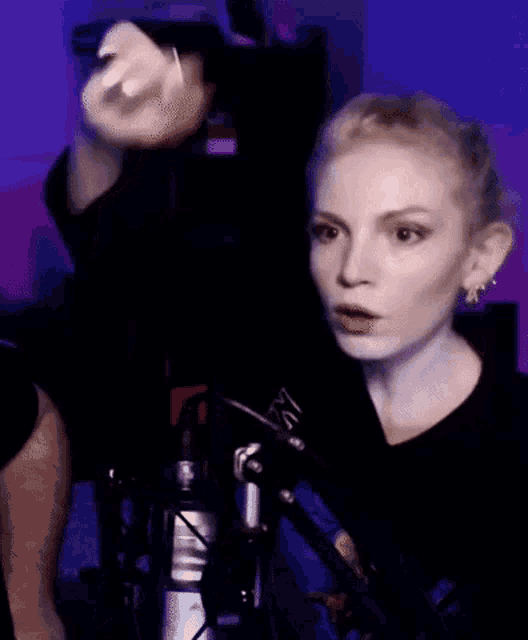 a woman is giving the middle finger while standing in front of a microphone in a dark room .