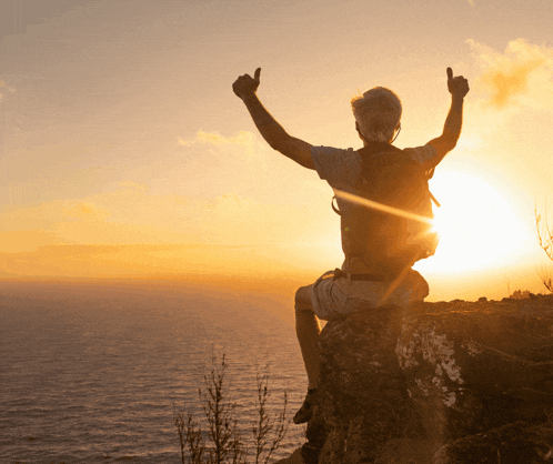 a man with a backpack is sitting on a rock with his arms in the air